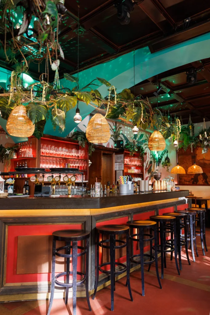 Bar with red counter, bar stools and hanging plants in the restaurant at Let's Be Frank Vienna