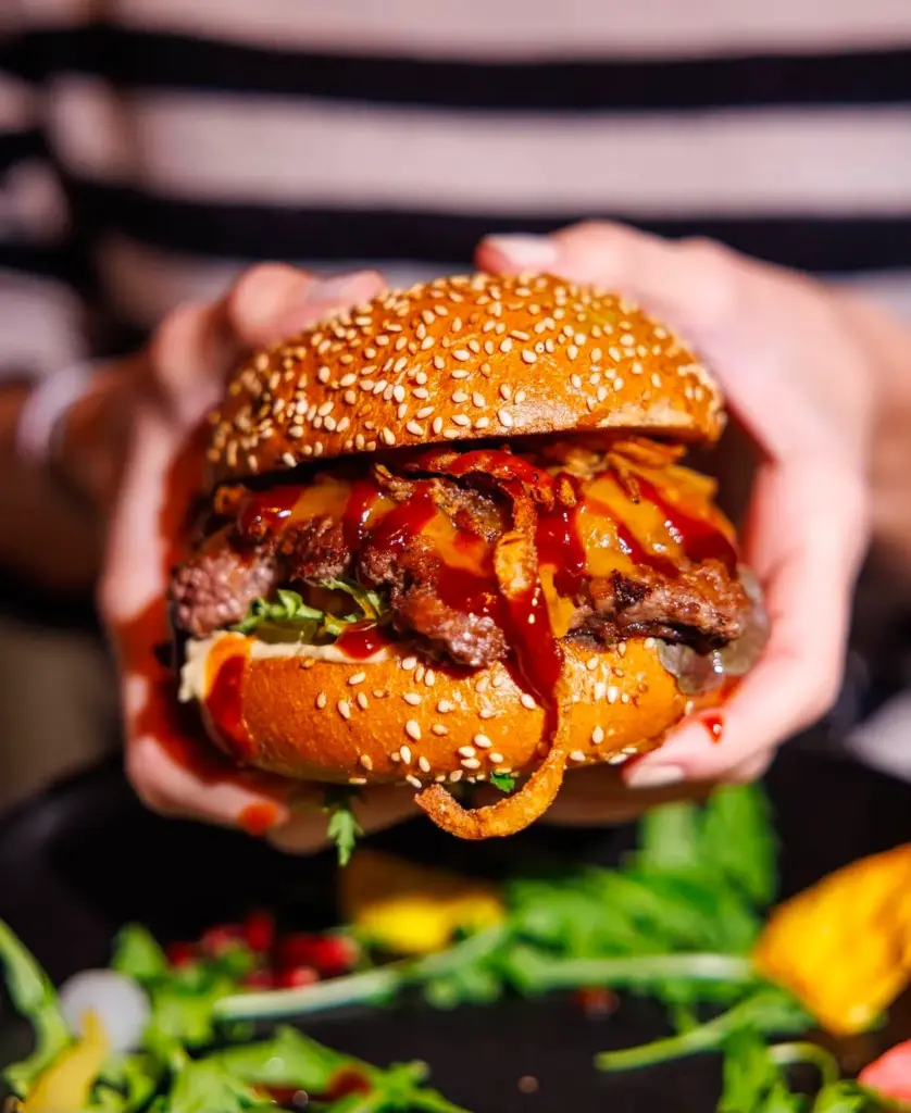 Hands holding a juicy burger over a fresh salad